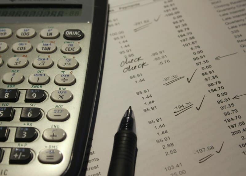 Close-up of a calculator, pen, and financial documents with handwritten notes and checkmarks, symbolizing financial accountability in remote teams.
