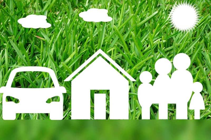 White cut-out icons of a car, house, family, sun, and clouds placed on green grass, symbolizing life insurance protection for family, home, and vehicle.